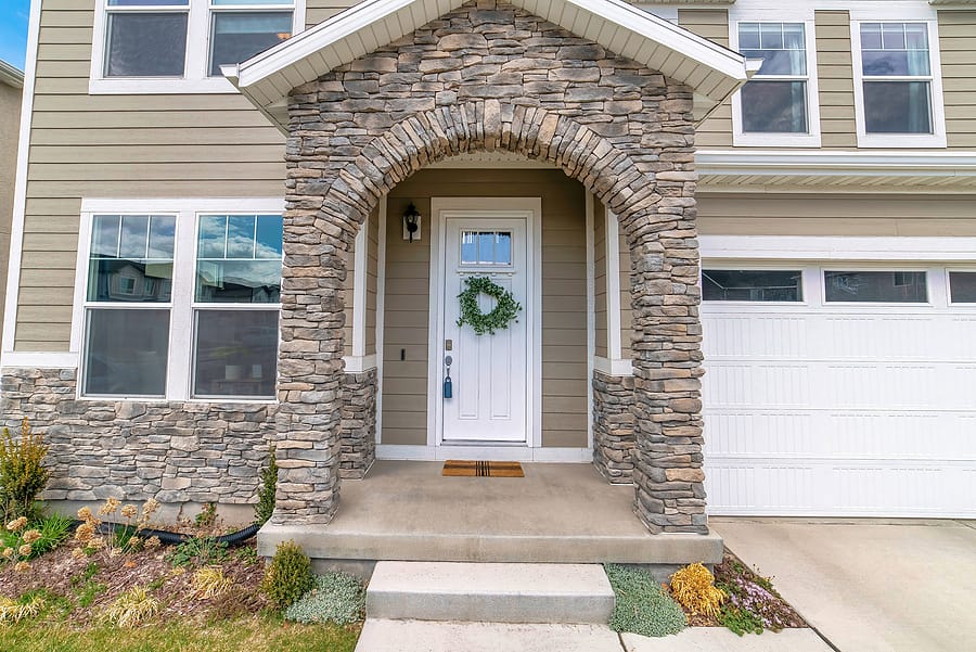 Beautiful facade of home with arched stone entrance and glass paned front door.