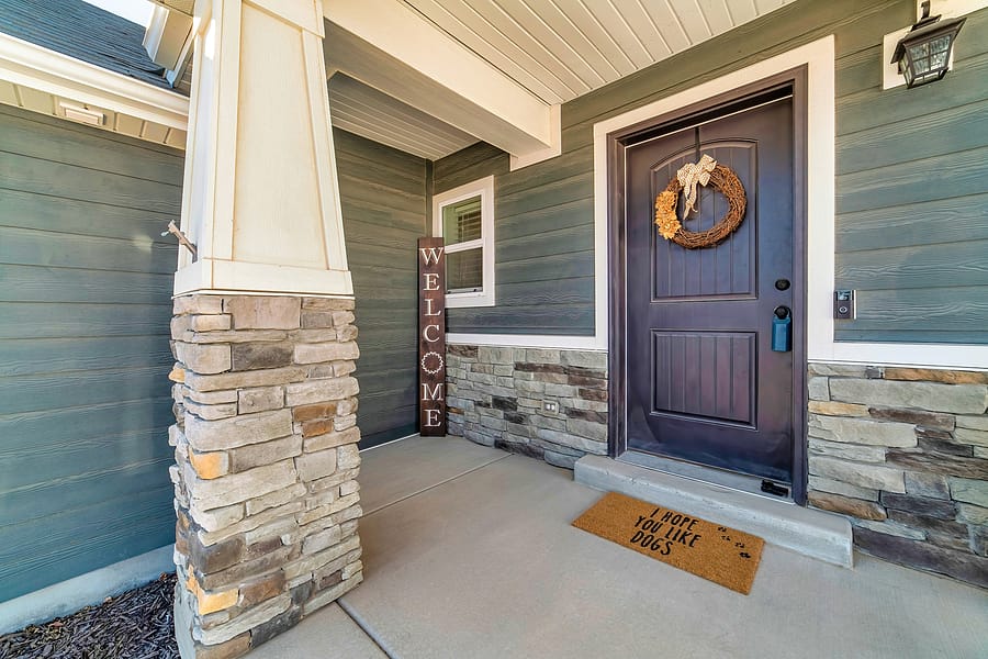 Open porch at home facade with stone wall wood siding and wreath on front door
